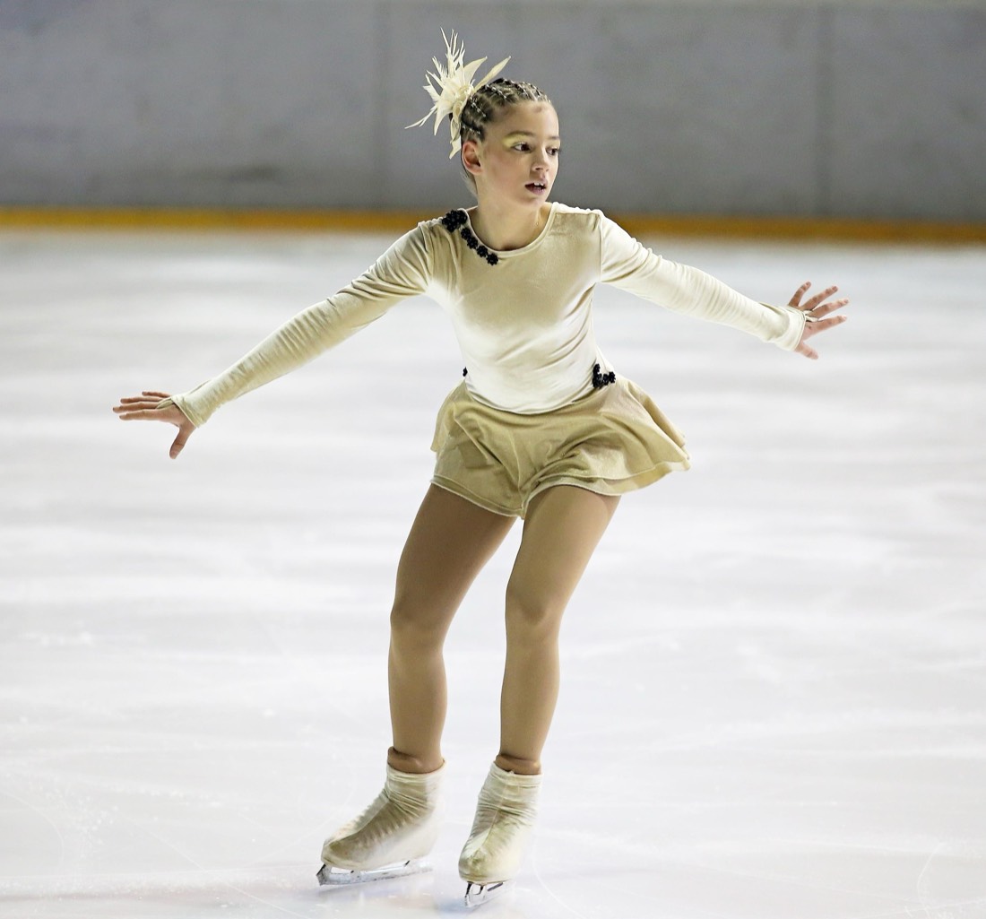 A young figure skater gliding across the ice with arms extended